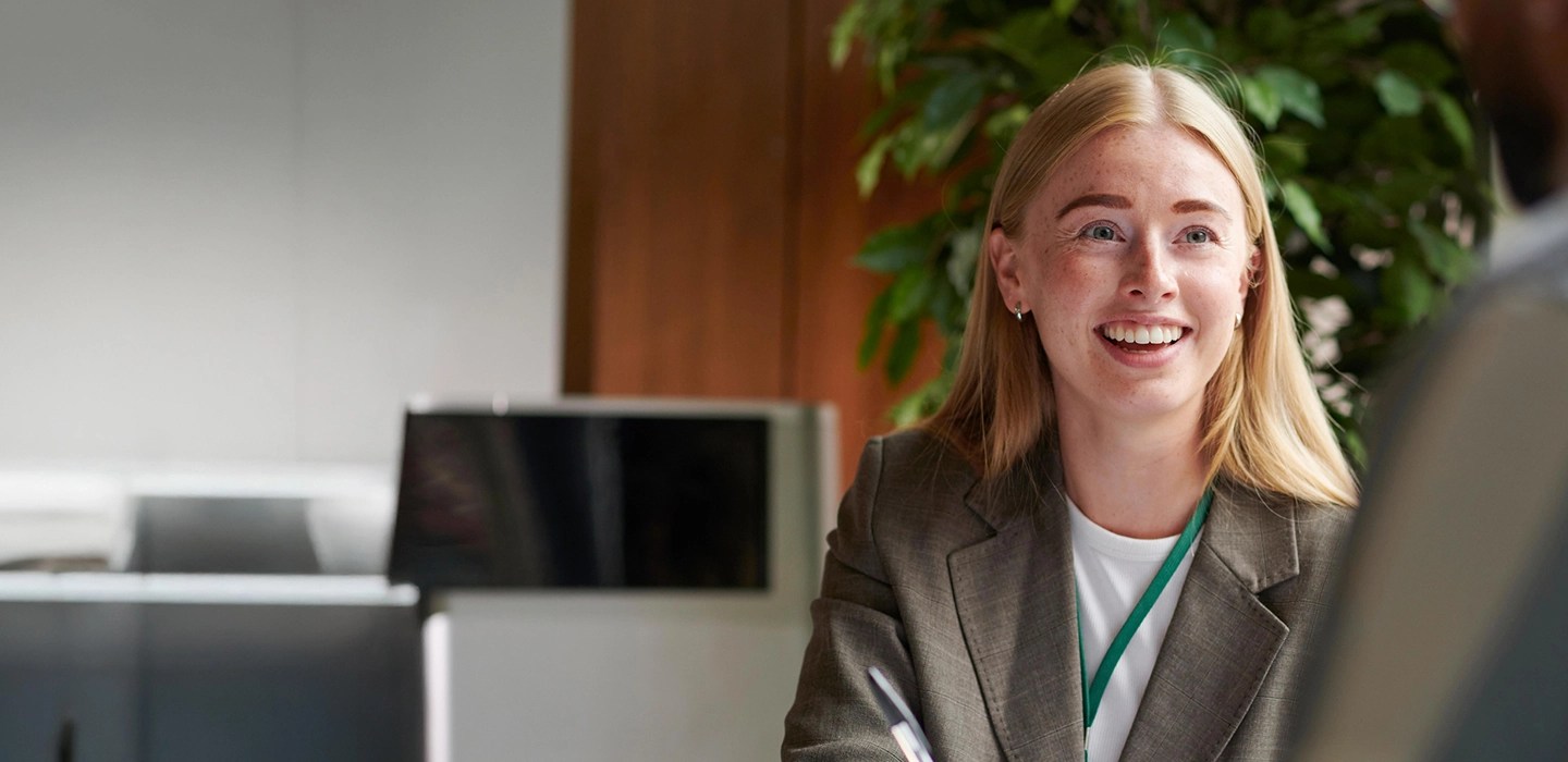 Close-up of a smiling businesswoman with long blonde hair and a grey blazer, taking notes.
