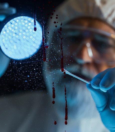 Close-up of a forensic scientist wearing a white protective suit and glasses in a dark room, holding a flashlight and swabbing bloodstains off a glass.