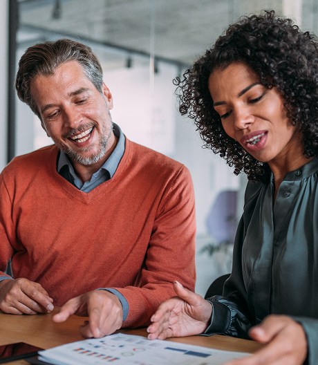 Two smiling professionals discuss printed notes with charts during a business meeting.