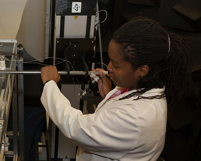 Female engineer in a white lab coat calibrating industrial testing equipment inside a manufacturing laboratory.