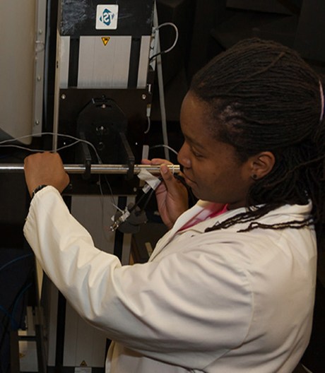 Female engineer in a white lab coat calibrating industrial testing equipment inside a manufacturing laboratory.