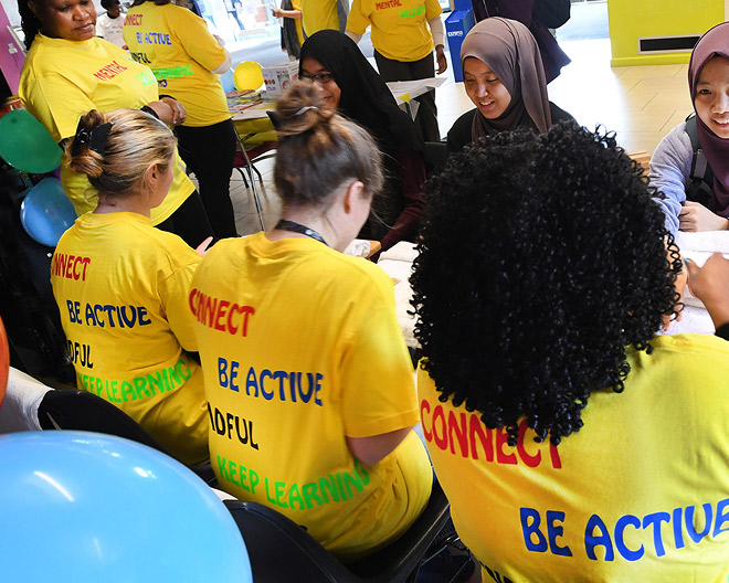 Diverse volunteers in bright yellow well-being T-shirts gather at a community health-promotion event.