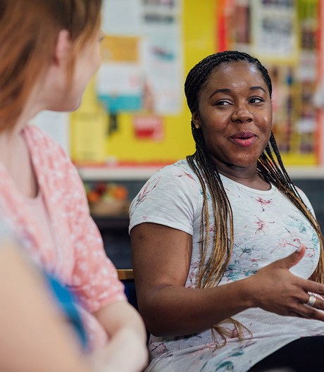 Woman sharing ideas during a small-group discussion on health behaviour change, gesturing while seated in a bright classroom.