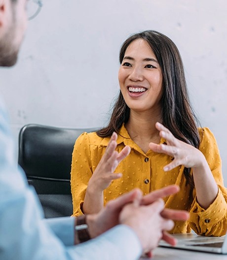 Smiling woman in a mustard-yellow blouse enthusiastically discusses ideas with a male colleague during an HR meeting.