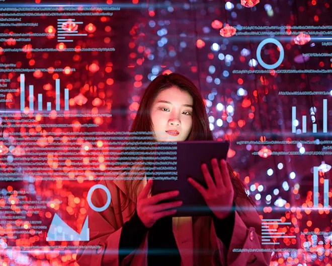 Woman holding a tablet is surrounded by vivid red-blue lights and semi-transparent charts, graphs and data streams floating in mid-air.
