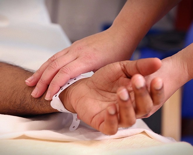 Close-up of a patient’s arm and hand wearing a hospital bracelet, gently held by a caregiver.