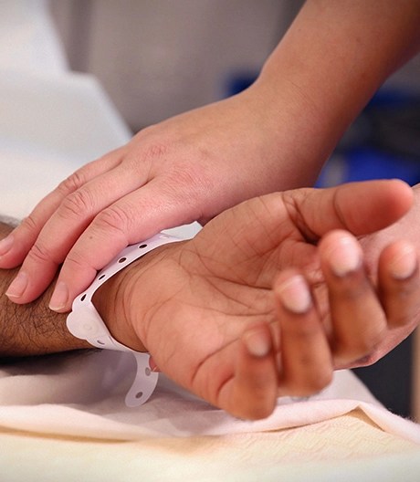 Close-up of a patient’s arm and hand wearing a hospital bracelet, gently held by a caregiver.