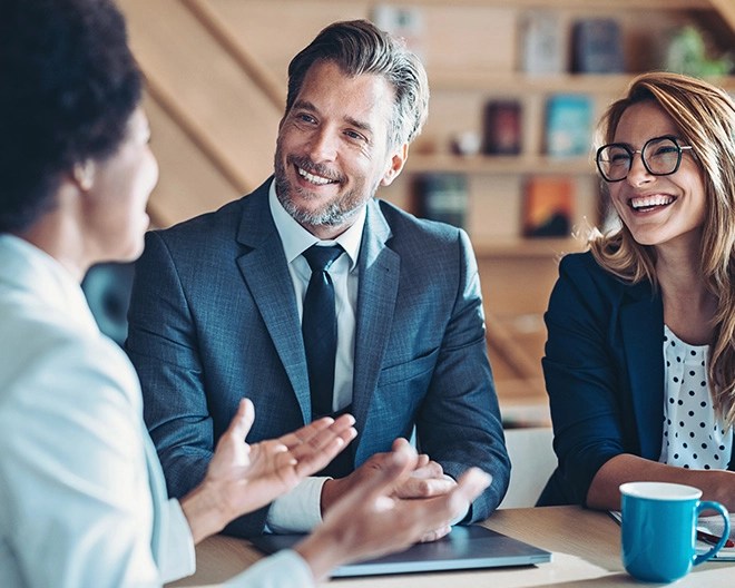 Business professionals in suits smiling and discussing strategy during an informal office meeting.