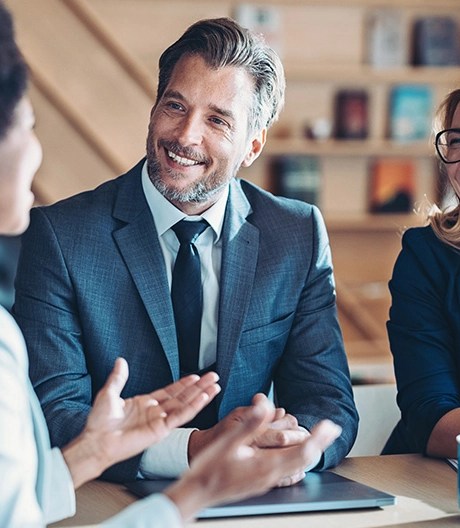Business professionals in suits smiling and discussing strategy during an informal office meeting.