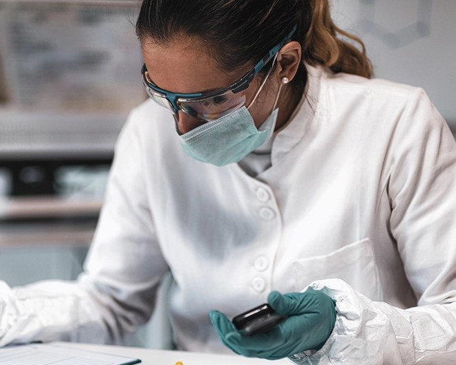Close-up of lab researcher wearing safety goggles and mask, analysing evidence.