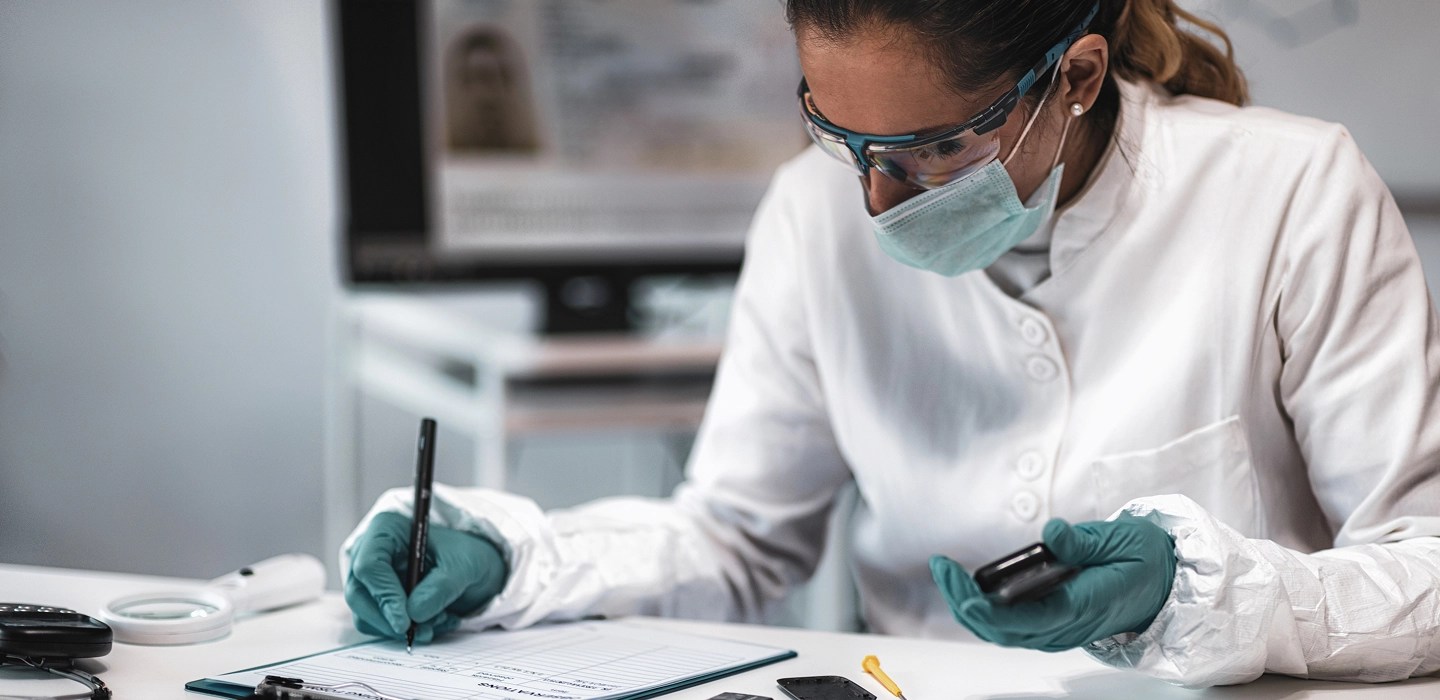 Close-up of lab researcher wearing safety goggles and mask, analysing evidence.