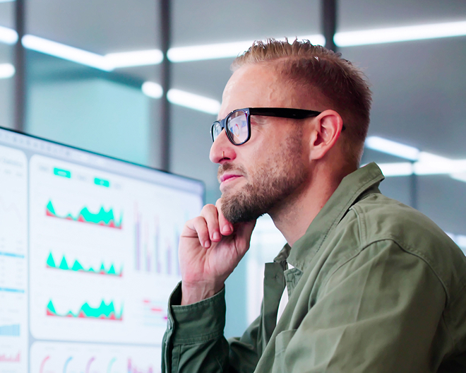 Financial professional seated at a desk, analysing economic charts and figures displayed on dual monitors in a well-lit office.