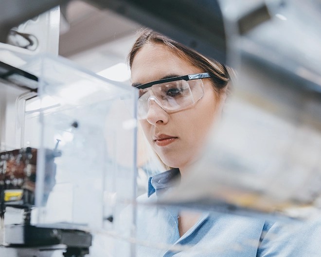 Close-up of a researcher wearing safety goggles in a laboratory, focused intently on their work with lab equipment slightly blurred in the background.