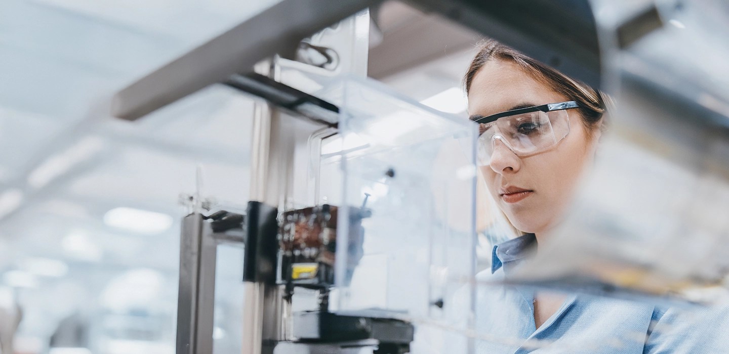 Close-up of a researcher wearing safety goggles in a laboratory, focused intently on their work with lab equipment slightly blurred in the background.