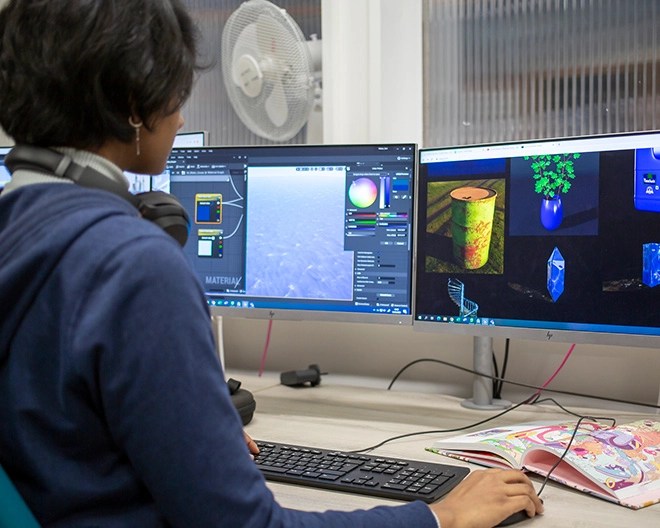 Game designer working on 3D renderings displayed across a dual-monitor computer setup.
