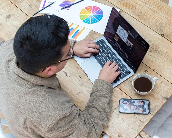 Bird’s-eye view of a marketing professional working on a laptop, surrounded by papers with colourful charts scattered across the desk.