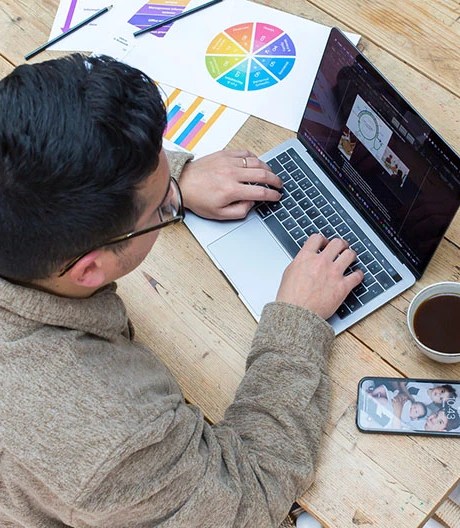 Bird’s-eye view of a marketing professional working on a laptop, surrounded by papers with colourful charts scattered across the desk.
