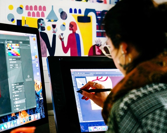Close-up of an art designer using a dual touchscreen monitor with design software, colourful graphics visible on the screens.