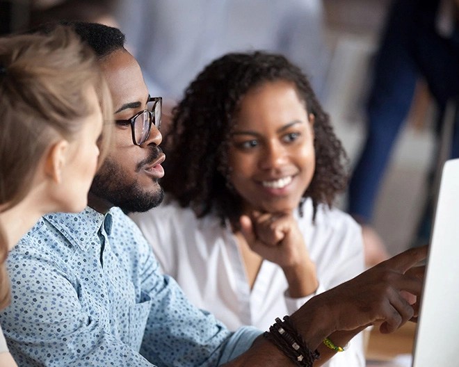 Close-up of three business students collaborating on a project, with one student pointing at a laptop screen.