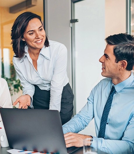 Four coworkers in business casual clothing smile and engage in discussion during a meeting in a bright office.
