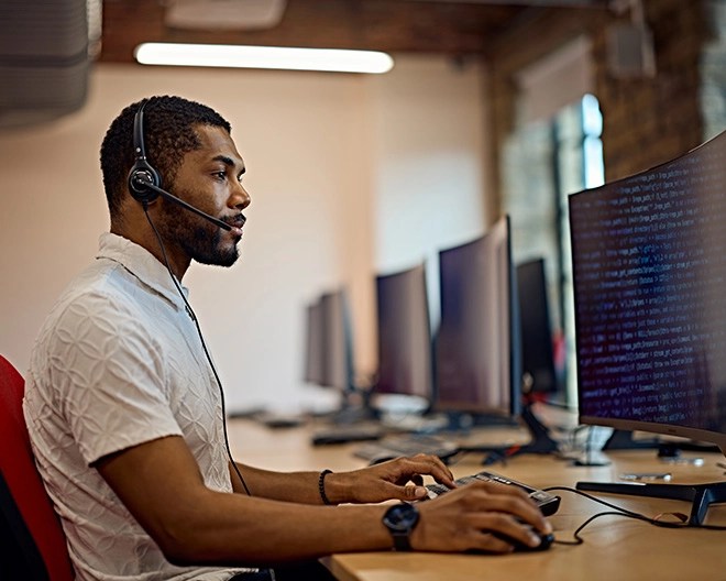 IT professional with a headset looks at code on his computer monitor.