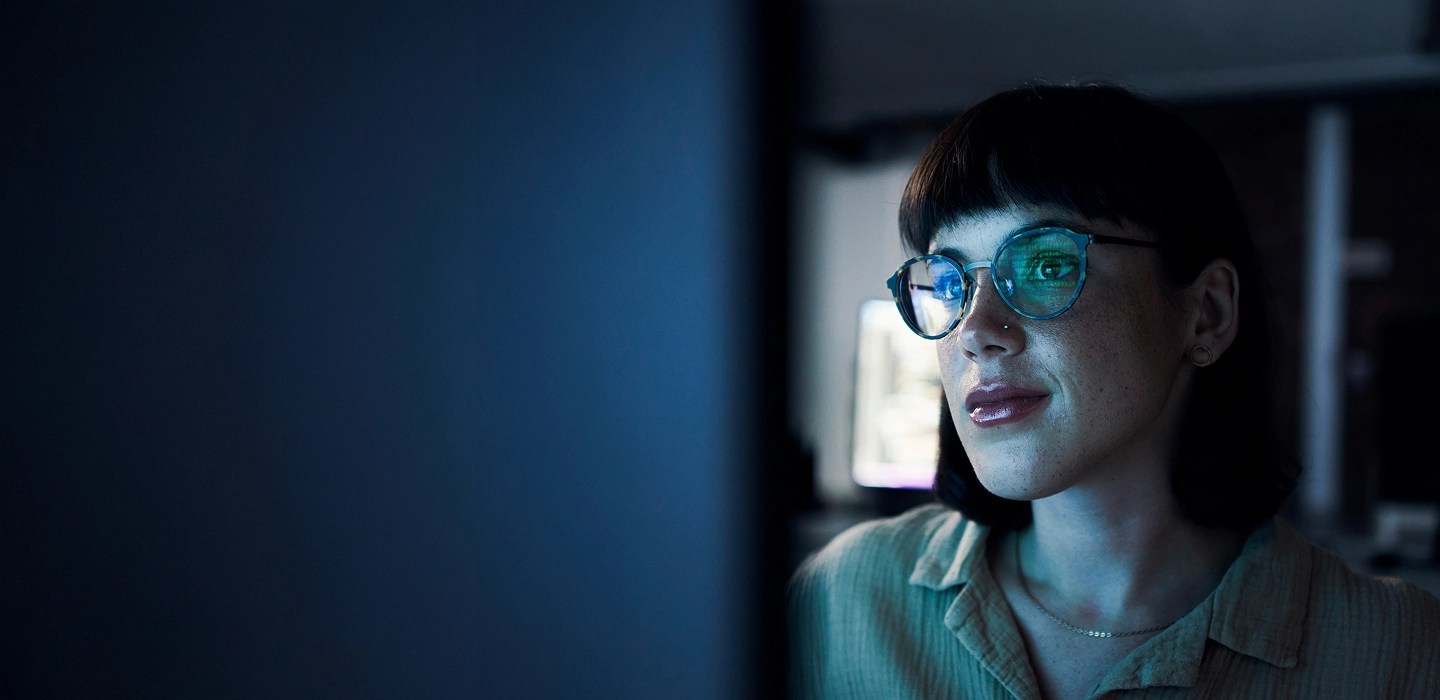 A woman looking at a monitor screen, with the reflection of code visible in her glasses.