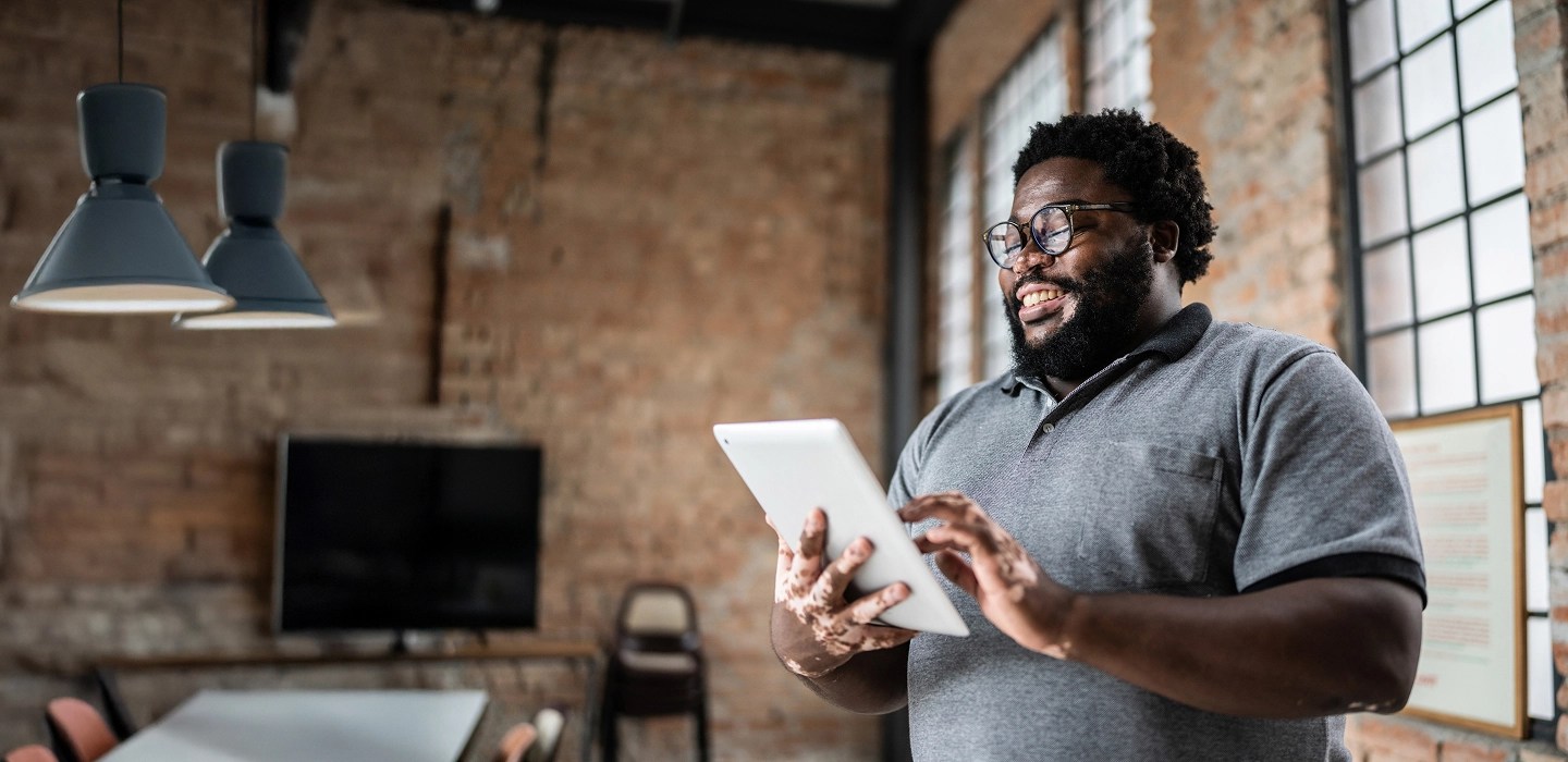 Cheerful professional standing and working on a tablet in a bright room with exposed brick walls.
