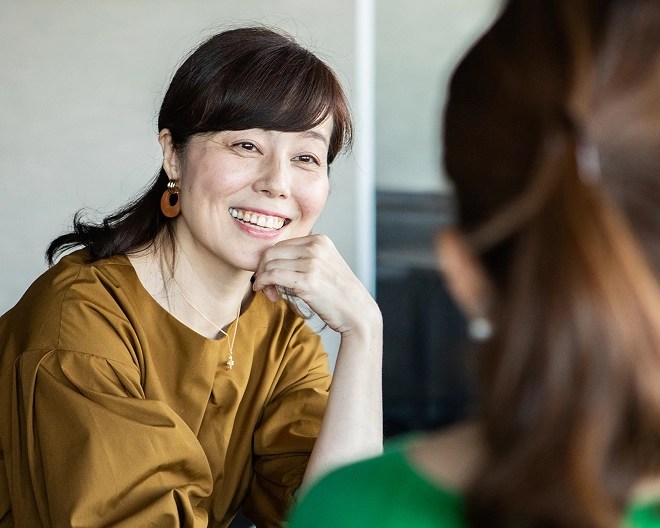 Smiling psychologist wearing a gold top, resting her hand on her chin while listening attentively to a client dressed in green.