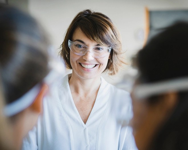 Close up of a science teacher with short hair, smiling and wearing safety goggles.