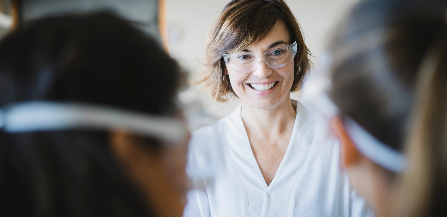 Close up of a science teacher with short hair, smiling and wearing safety goggles.