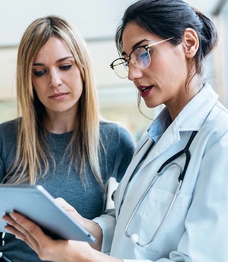 Researcher wearing a white lab coat and a stethoscope reviews results on a tablet with a colleague.