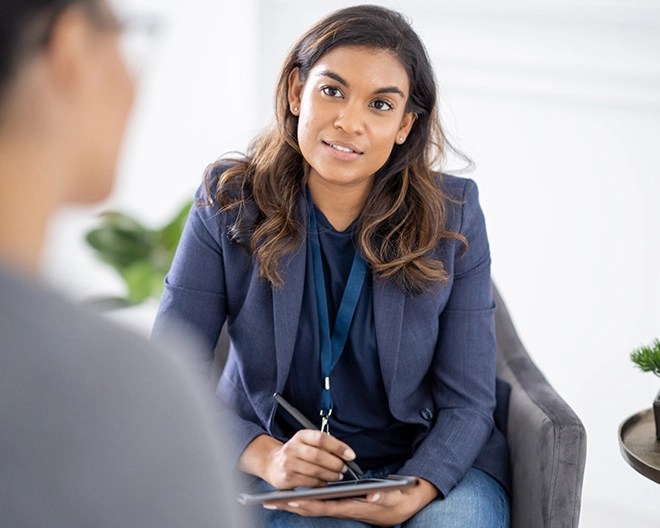 Team leader in business casual attire, listening attentively to a colleague while taking notes on a tablet.