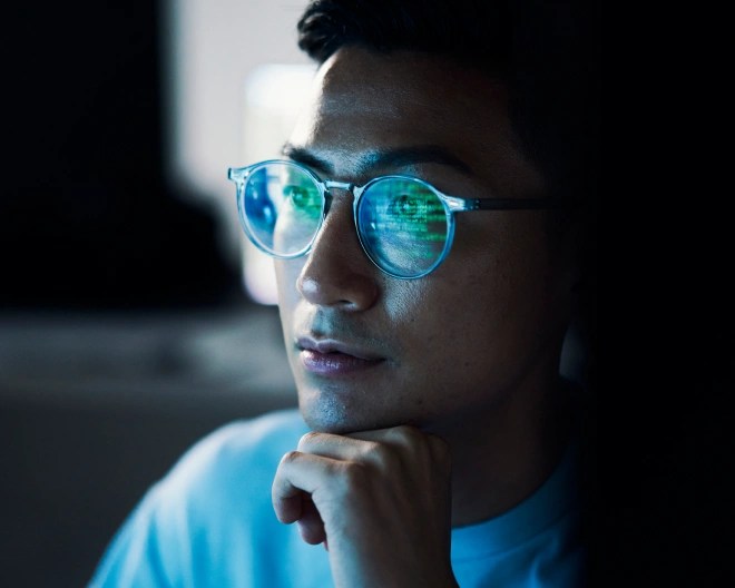 man looking at a computer with the screen reflected in his glasses