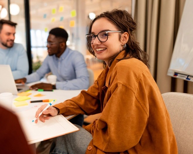 woman sat with male colleagues. She is smiling and taking notes