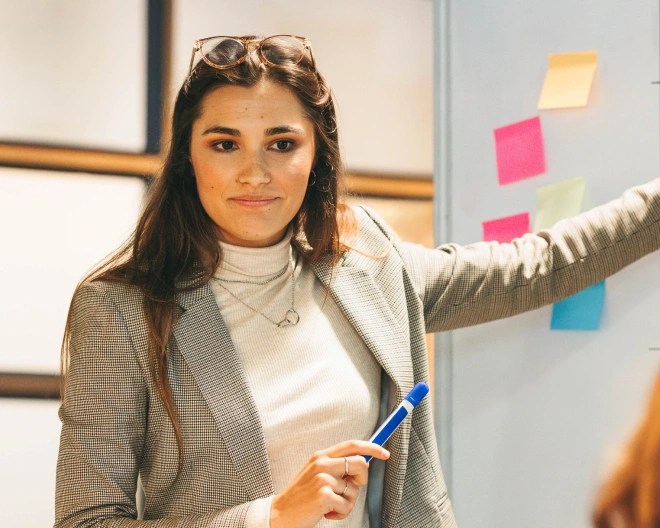 woman pointing at a whiteboard with post-it notes on it