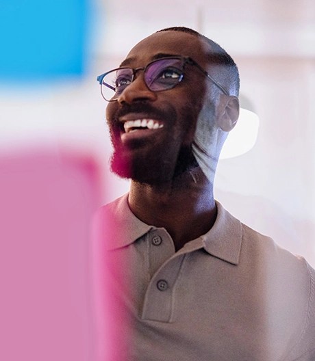 A man in glasses looking at sticky notes on a glass window, smiling.