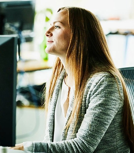 A woman in a grey cardigan sitting at a desk in front of a monitor.