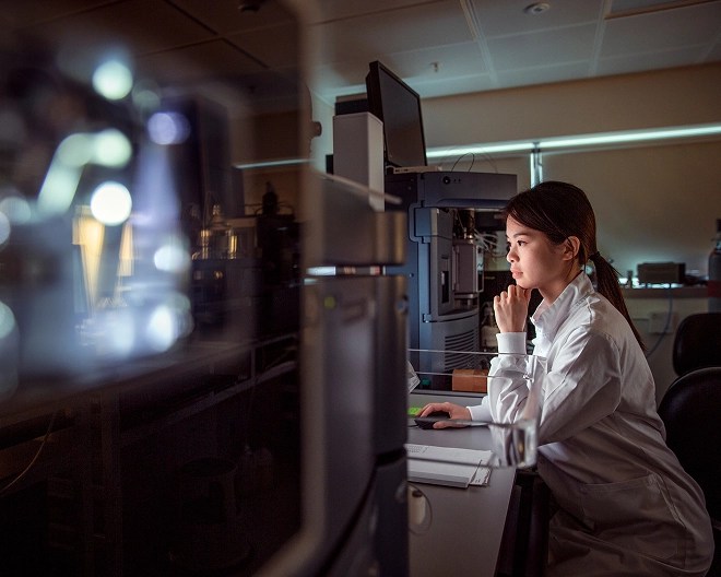 Researcher in a lab coat reviewing evidence on her computer screen in a dimly lit office.