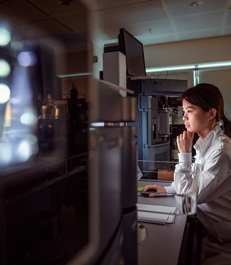Researcher in a lab coat reviewing evidence on her computer screen in a dimly lit office.