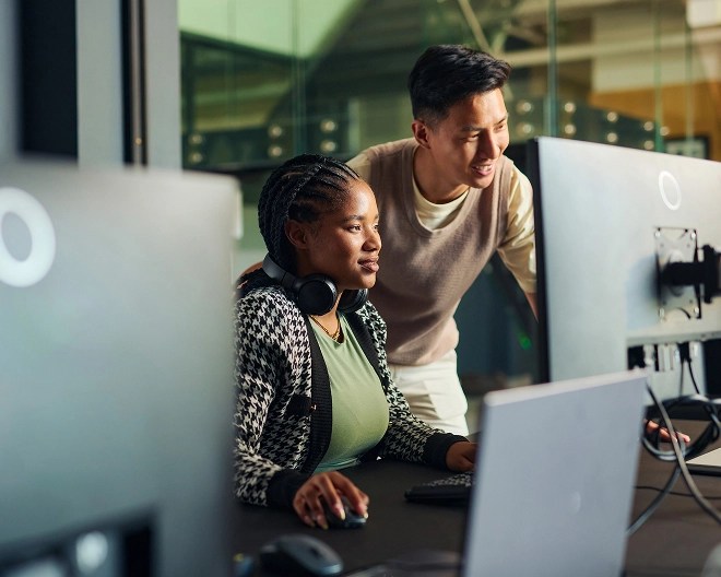 Two colleagues dressed in casual clothes work together behind a computer in a tech office.
