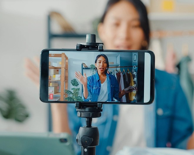 Close-up of a phone capturing a content creator waving and making a video.