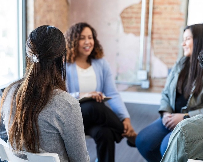 Group counselling session in a bright, modern space, with a smiling therapist leading the discussion among participants.