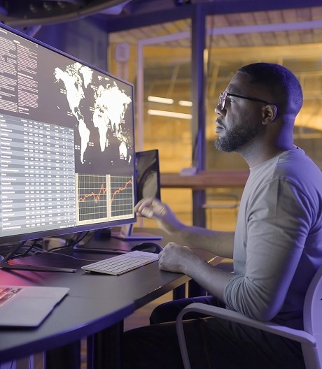 Data scientist analyzing numbers, charts, and a global map on a desktop computer at night, with the screen casting a soft glow in a dark room.