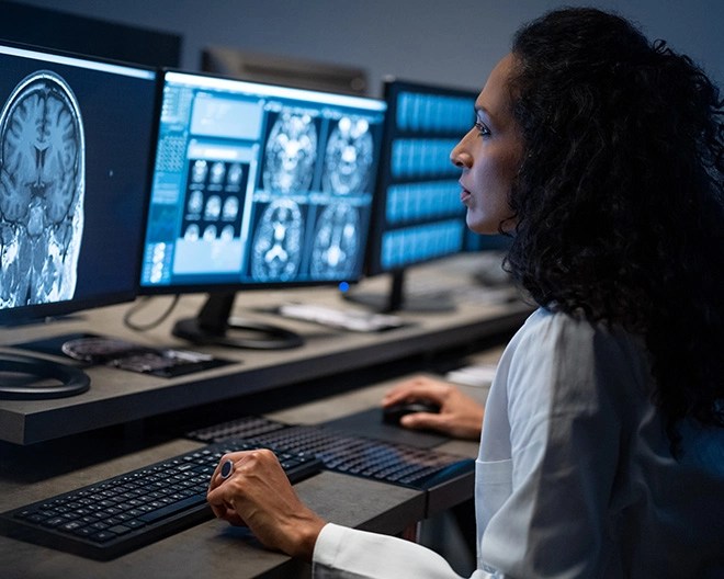 Neuroscientist reviews brain scans on a computer monitor in a dimly lit lab.