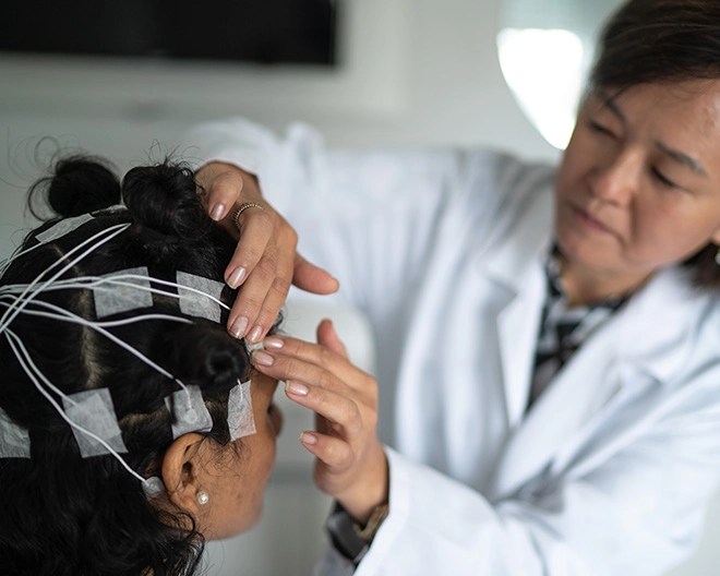 Neuroscientist in white coat fits a brain scanning device on patients head.