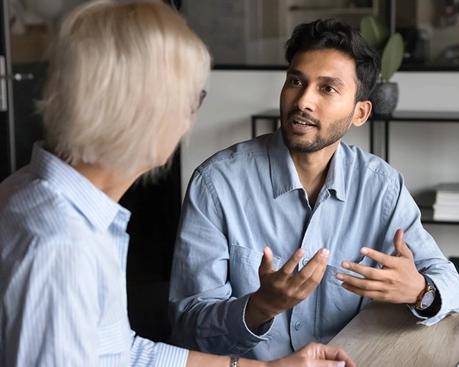 Two colleagues wearing business attire gesture with their hands as they discuss a business topic.