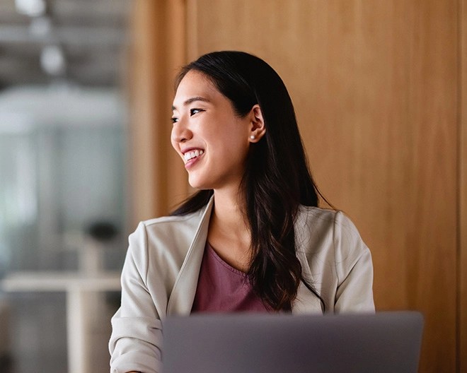 Businesswoman with long curly hair smiling and looking off to the side in an office space.
