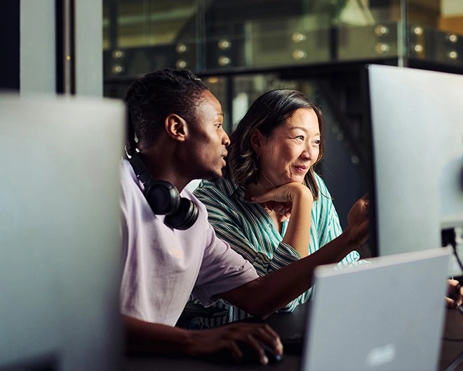 Two colleagues engaged in discussion while looking at a computer screen together.