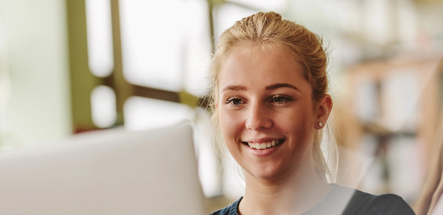 A woman wearing a black jumper smiling at a laptop screen.
