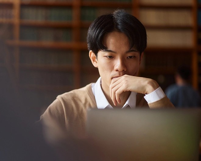 A student wearing a light brown jumper over a white shirt, looking at a laptop screen.